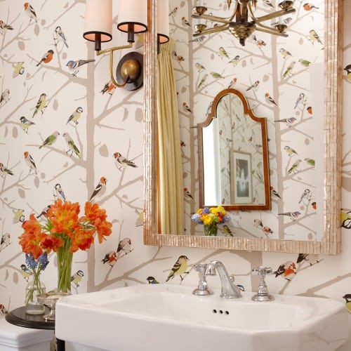 White petal stool sink with mirror hung above it surrounded by nature themed wallpaper
